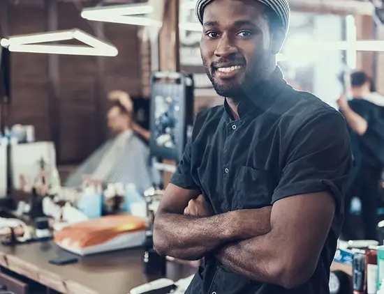 Smiling barber standing with folded arms inside a barbershop